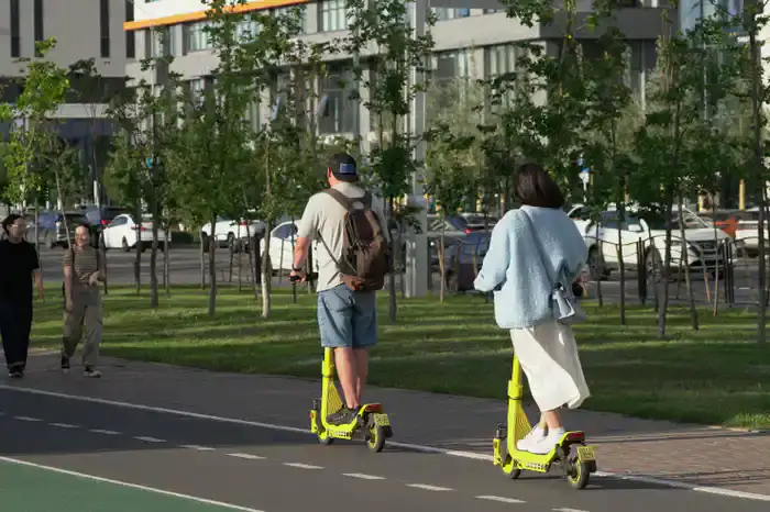 Парень и девушка на электросамокатах едут друг за другом без шлемов, Астана