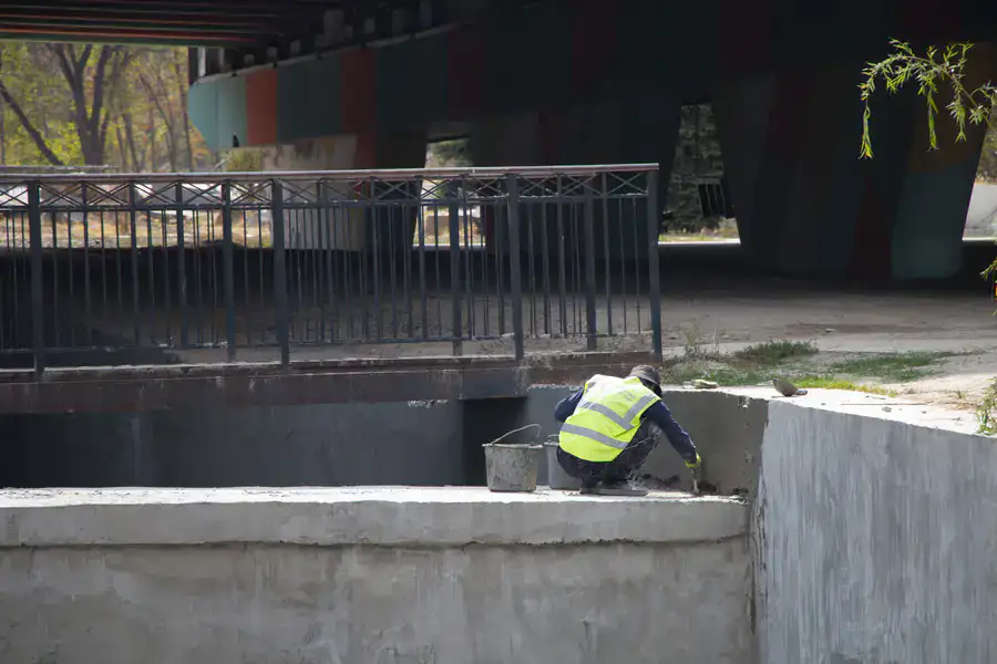 рабочий шпаклюет бетонное русло реки, реконструкция Большой Алматинки